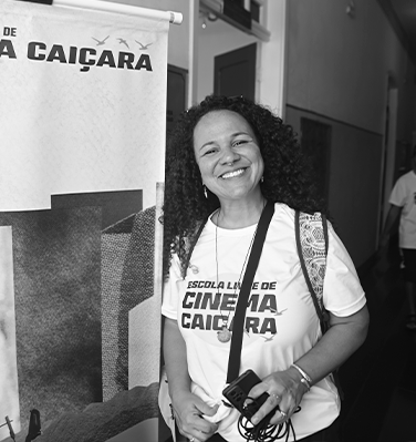 Sou uma mulher cis, branca, de 39 anos. Tenho os cabelos cacheados e compridos, estou sorrindo e usando uma camiseta onde está escrito Escola Livre de Cinema Caiçara.