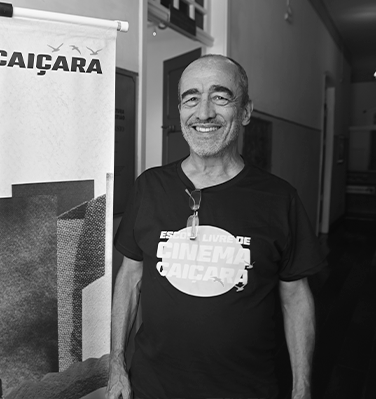 Sou um homem branco, com 65 anos, um tanto calvo, barba aparada, estou usando uma camiseta escuro com dizeres da Escola de Cinema Caiçara