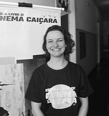 Sou uma mulher cis branca. Na foto estou sorrindo, tenho cabelos castanhos claros soltos para o lado e visto uma camiseta preta.